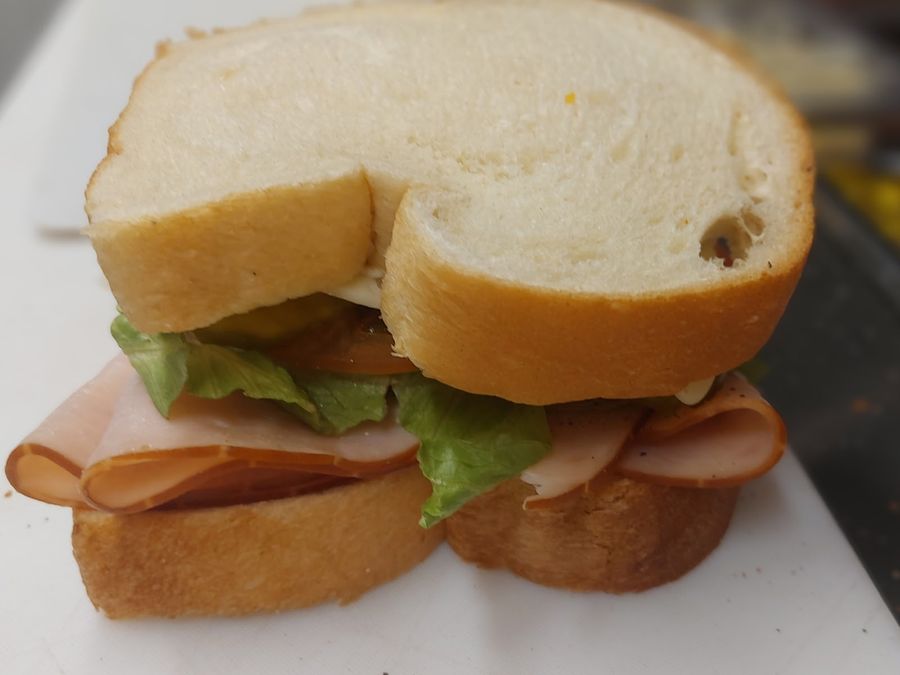 A deli sandwich on white bread with ham, lettuce and tomato