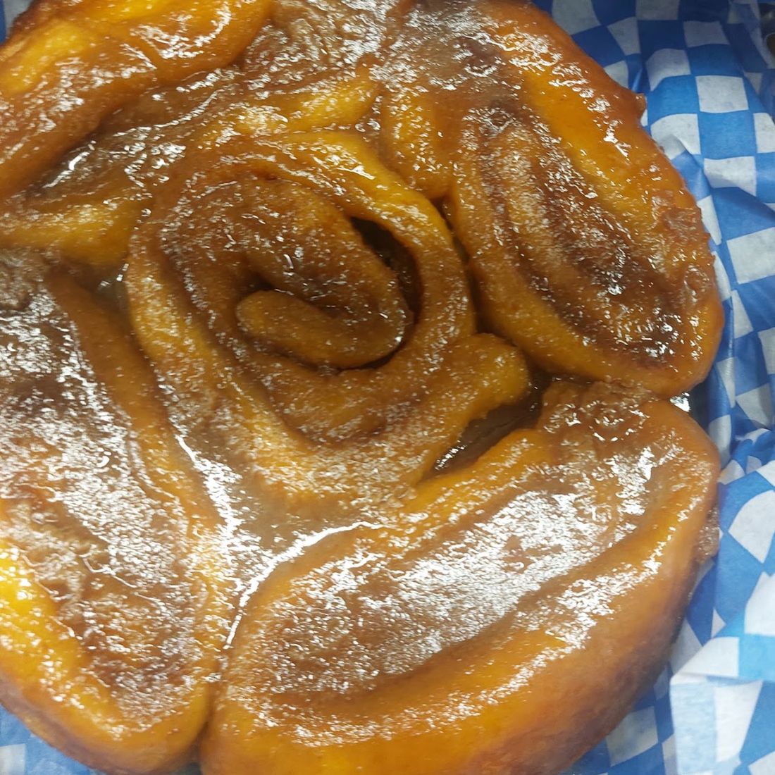 A sticky bun on blue-check paper, the caramelized maple sauce running over the top