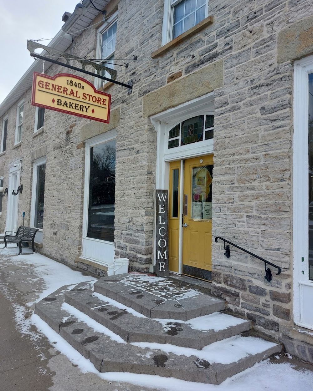The yellow front door and stone steps of the store, under the hanging sign